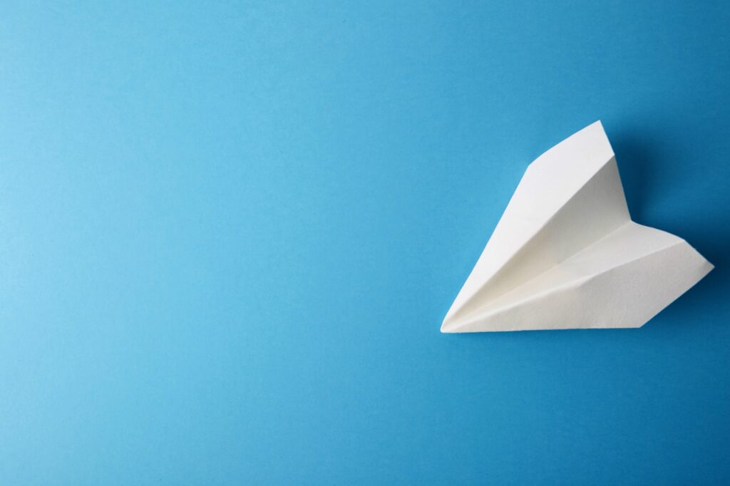 Flat lay of white paper plane and blank paper on pastel blue color background.Horizontal.